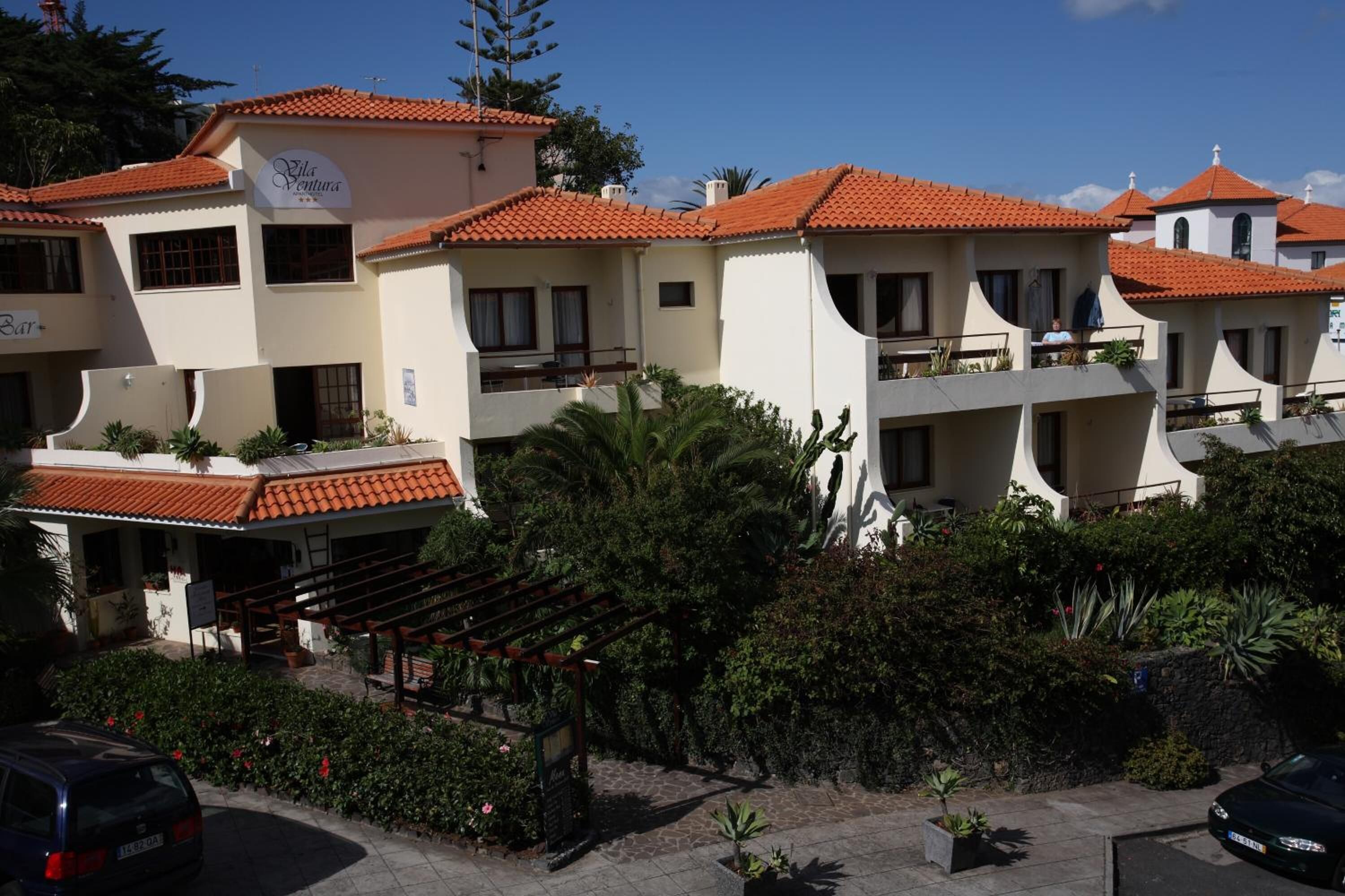 A hotel with multiple buildings, each with red-tiled roofs and balconies. There is a sign that reads "Villa Venturas" and a bar area with outdoor seating.