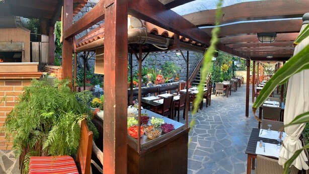 An outdoor restaurant with brick walls, a brick fireplace, and a covered patio area with tables and chairs. - Vila Ventura Apartment Hotel (Santa Cruz)