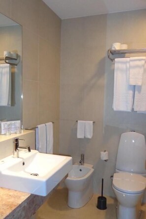 Et badeværelse med vask, bidet, toilet og et spejl.