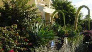 A two-story building with a stone wall and lush greenery. - Vila Ventura Apartment Hotel (Santa Cruz)