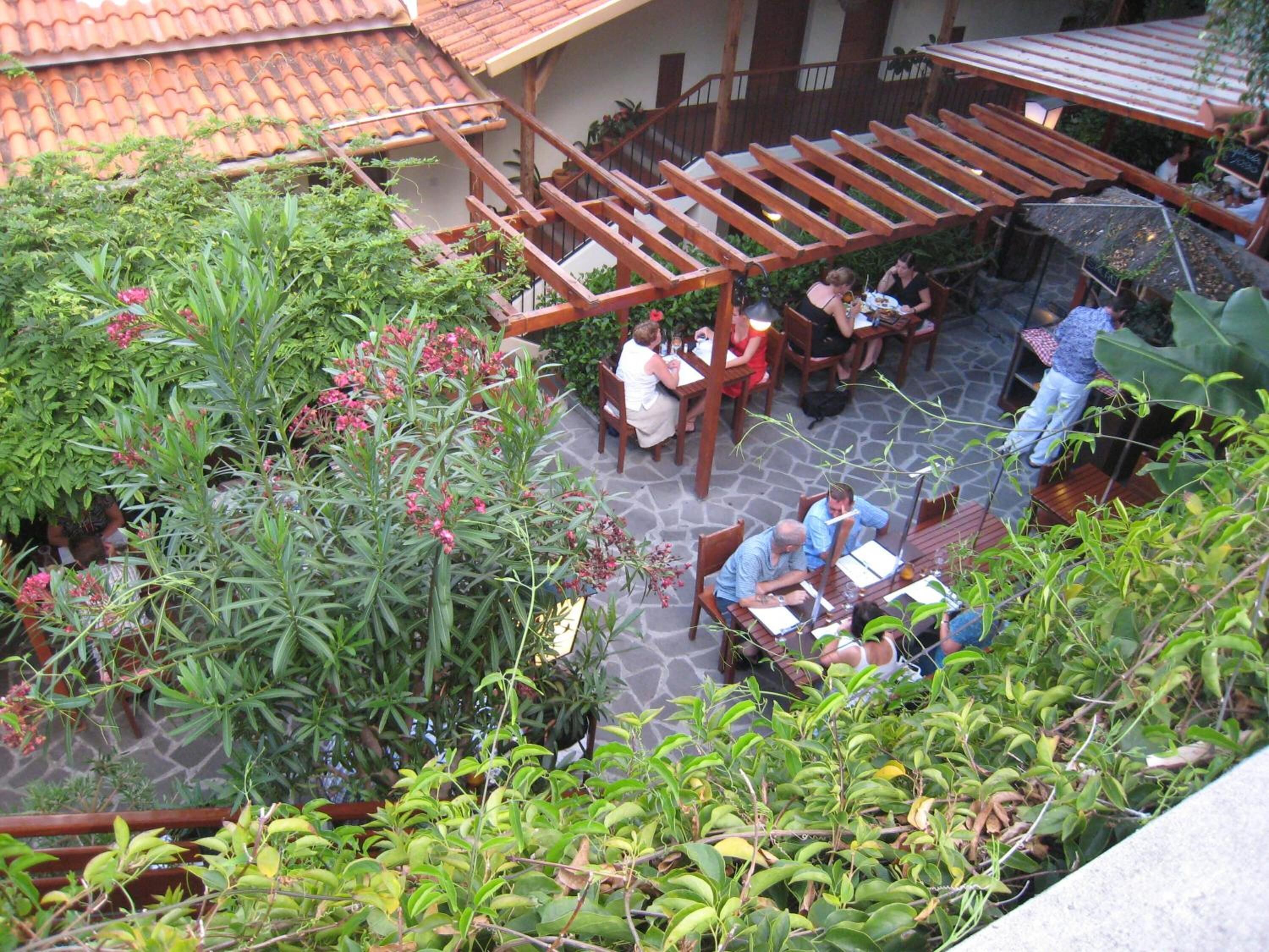 An outdoor patio area with wooden furniture and tables, surrounded by lush greenery and plants.