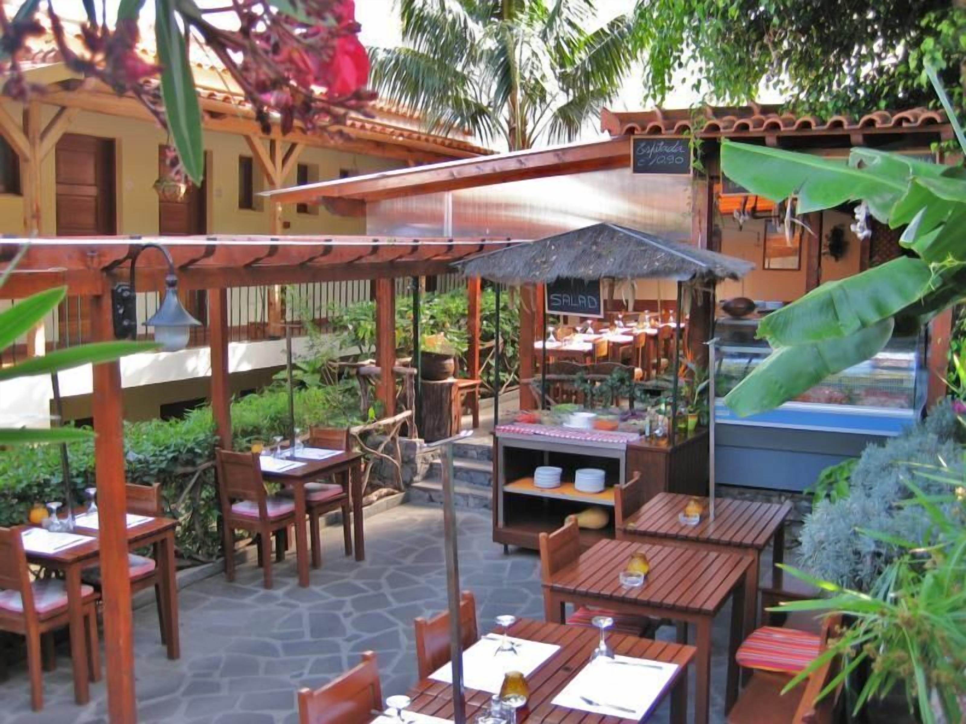 An outdoor dining area with wooden tables and chairs, a covered seating area, and a food display counter.