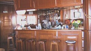 A bar area with wooden cabinets, a countertop, and bar stools. - Vila Ventura Apartment Hotel (Santa Cruz)