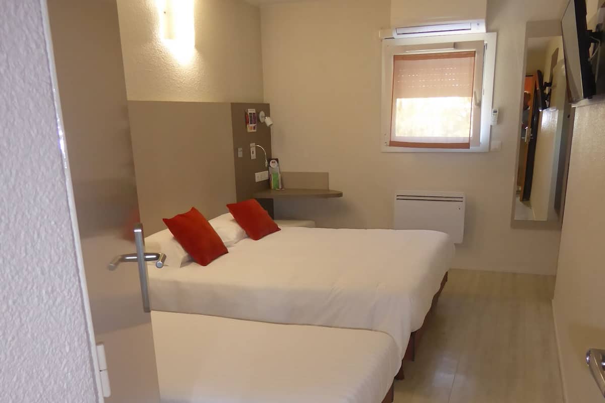Une chambre d’hôtel de taille réduite, comprenant deux lits simples, une petite salle de bain et une kitchenette.