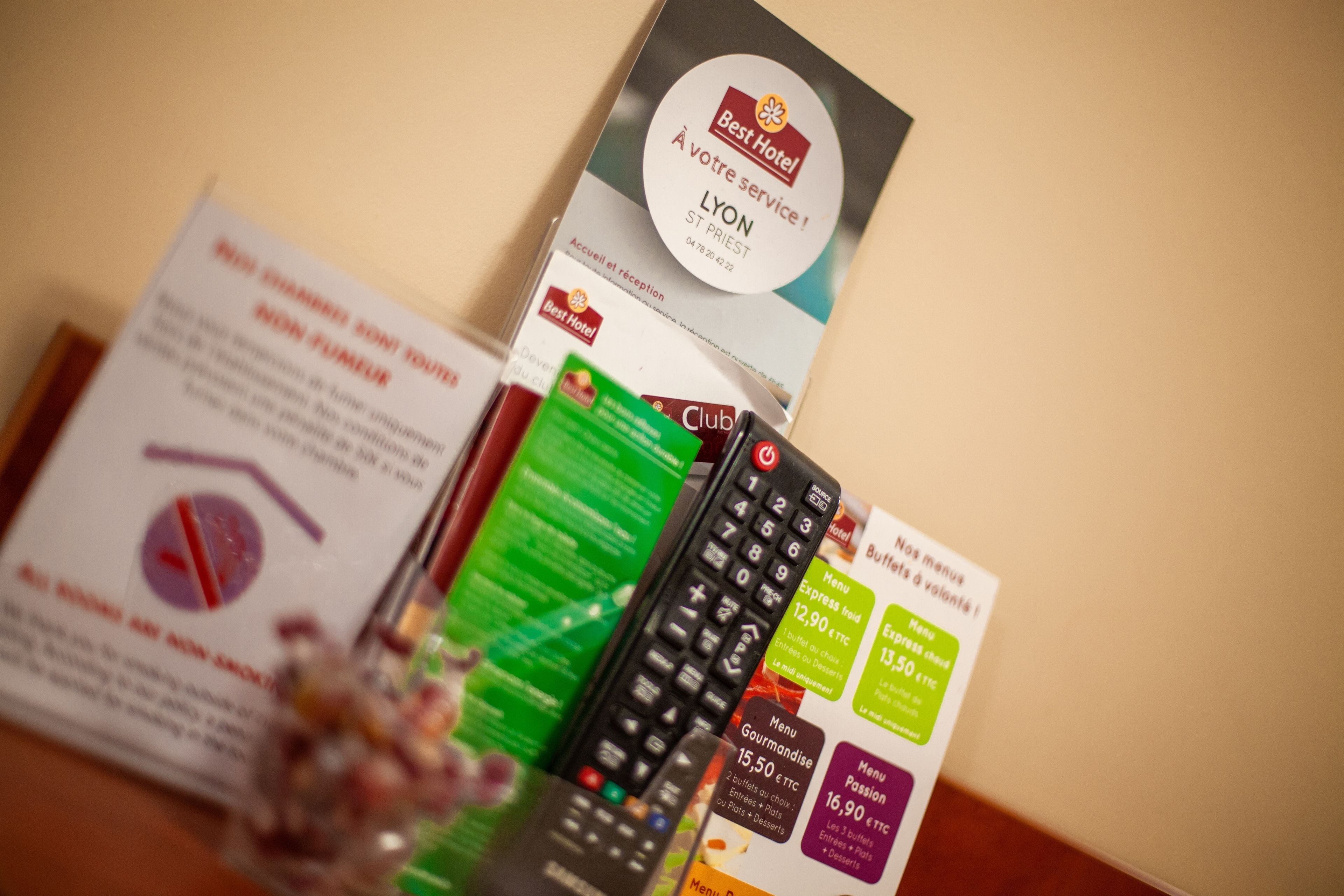 A Best Hotel Lyon brochure, a menu, and a remote control on a table.