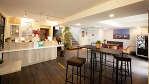 A modern reception area with a wooden counter, bar stools, and a seating area with a sofa and chairs. - Best Hotel Lyon St Priest (Saint-Priest)
