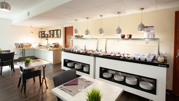 A modern dining area with a buffet setup, including a counter with various food items and a seating area with tables and chairs. - Best Hotel Lyon St Priest (Saint-Priest)