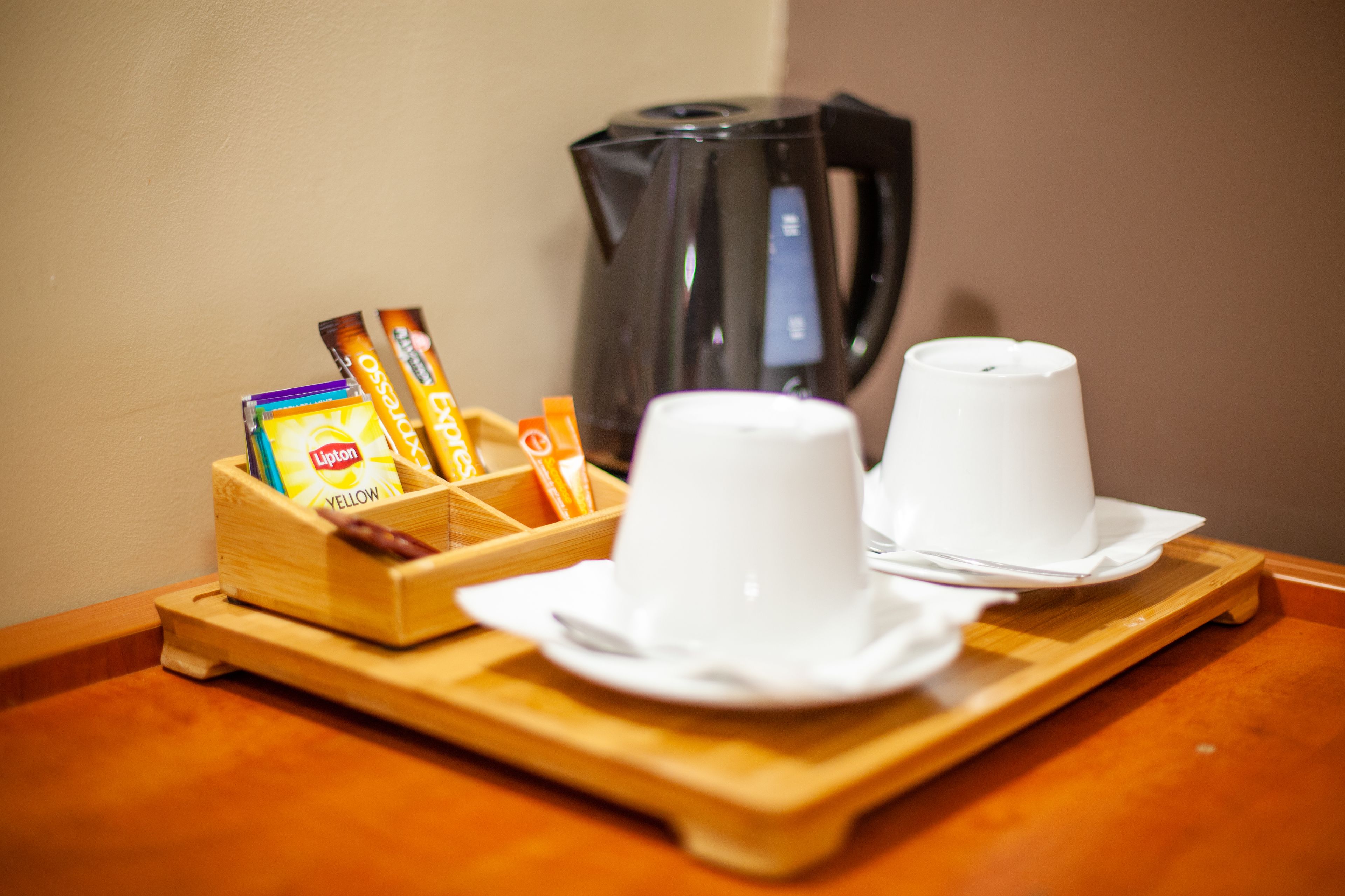 Una bandeja de madera con dos tazas blancas y una caja de té Lipton sobre una mesa de madera.
