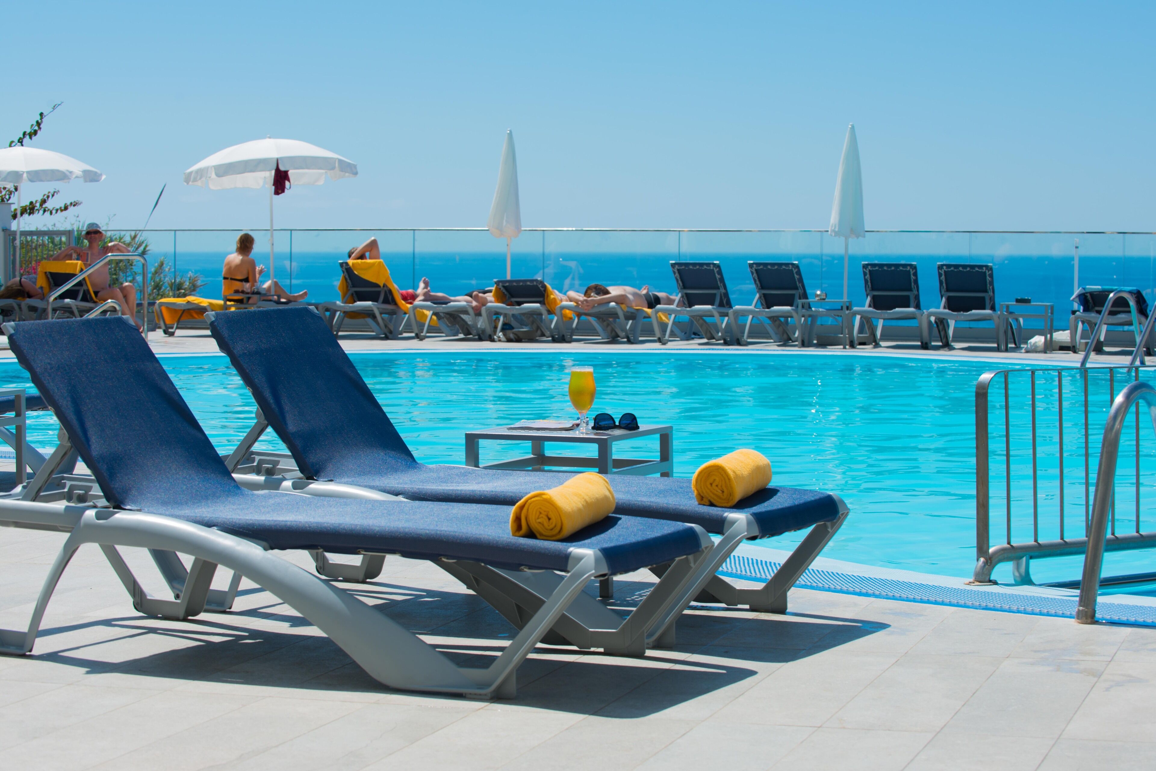 A poolside area with lounge chairs and umbrellas, a pool, and a clear view of the ocean.