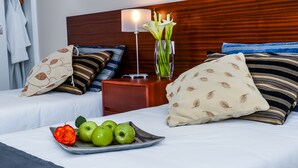 A hotel room with two beds, a bedside table with a lamp, a vase with flowers, and a tray with apples and a rose.