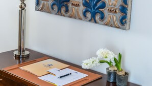 A desk with a decorative tile, a candle holder, a pen, papers, and two small potted plants.