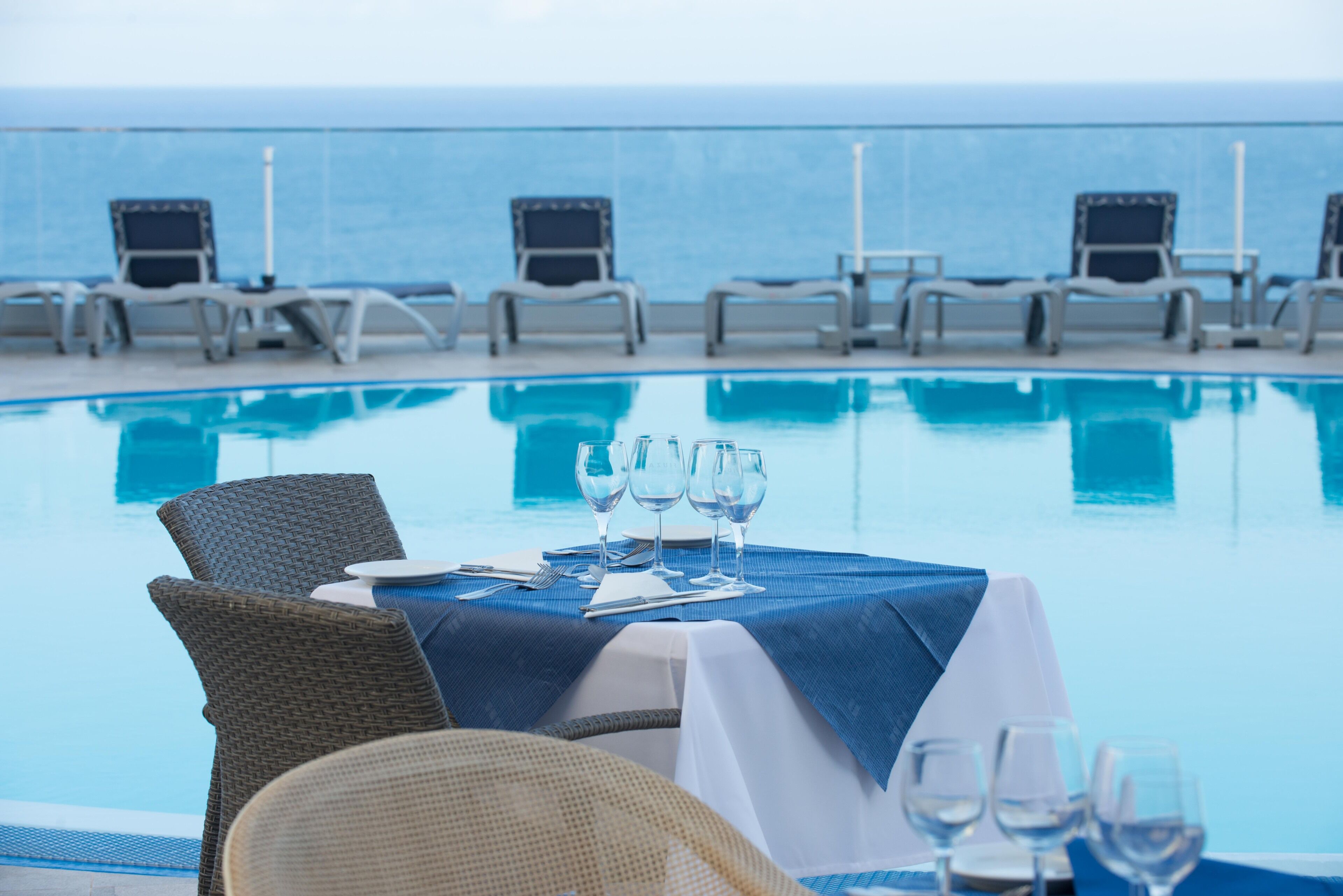 A poolside dining area with a table set for two, overlooking the ocean.