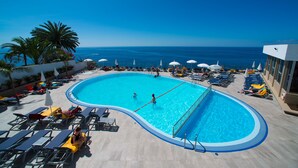 A swimming pool with a view of the ocean, surrounded by lounge chairs and umbrellas.