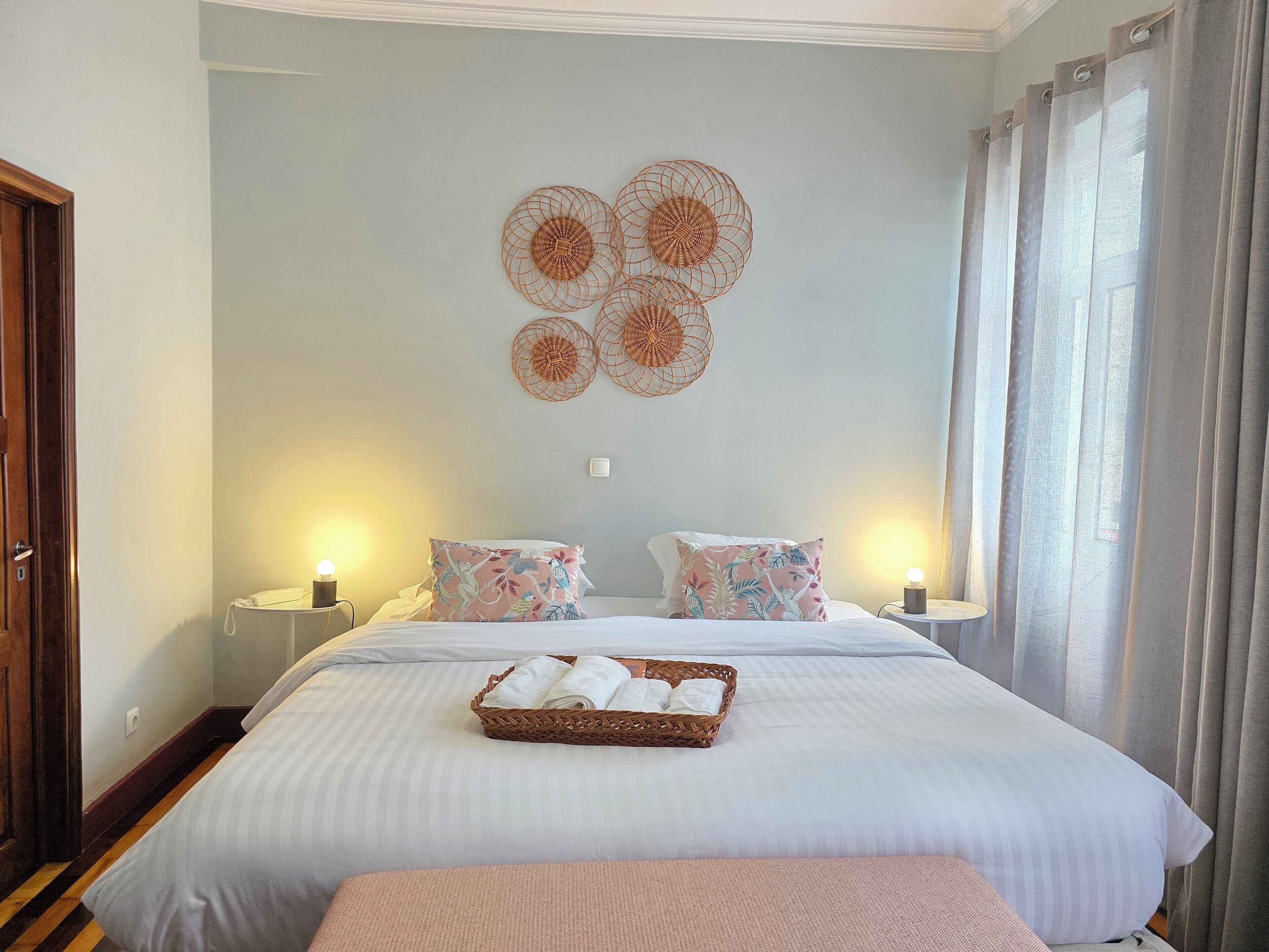 A neatly made bed with a basket of towels, two bedside lamps, and a wall decoration.