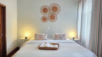 A neatly made bed with a basket of towels, two bedside lamps, and a wall decoration.