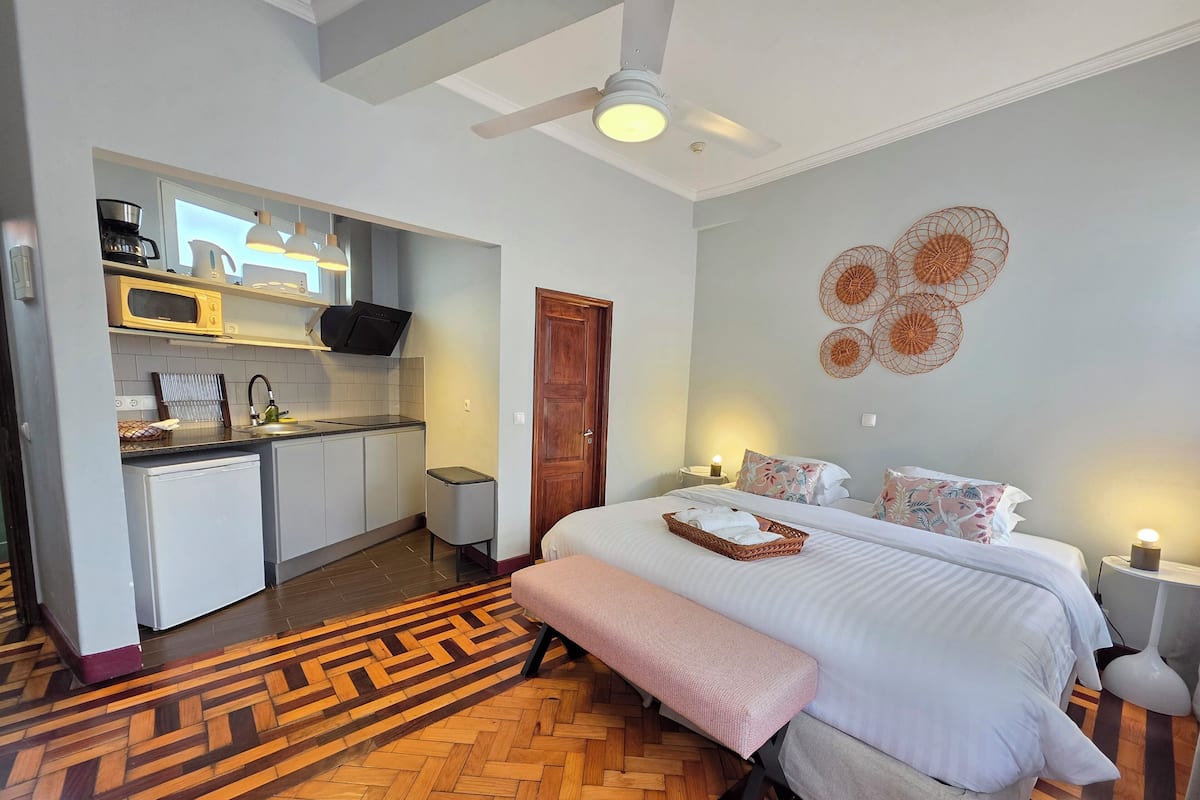 Une chambre d’hôtel compacte comprenant un coin cuisine, un lit avec une banquette et un sol à motifs en chevrons.