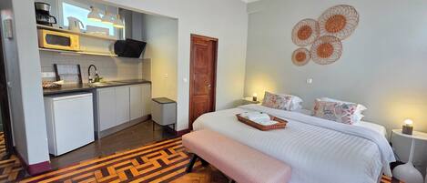 A compact hotel room with a kitchenette, a bed with a bench, and a patterned herringbone floor.