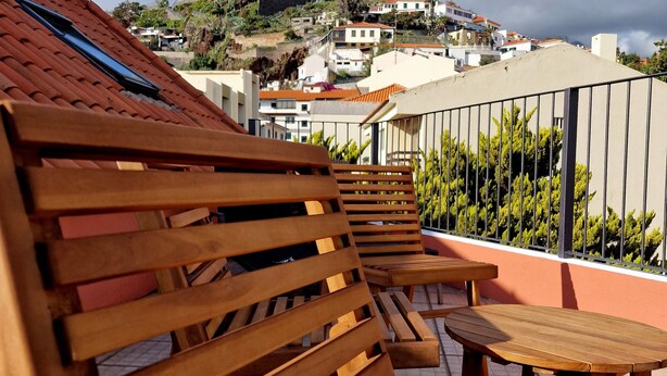A terrace with wooden furniture and a view of a castle on a hill. - ASPA Studios - Urban Conscious Living (Funchal)