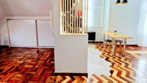 A modern room with a wooden herringbone floor, a white wall, a wooden partition with vertical slats, a black chair, a wooden table, and black pendant lights. - ASPA Studios - Urban Conscious Living (Funchal)