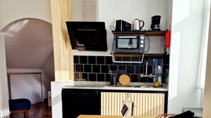 A compact kitchen with a microwave, toaster, and coffee maker. There is a wooden table with a bottle of liquor and a basket. The floor has a herringbone pattern. - ASPA Studios - Urban Conscious Living (Funchal)