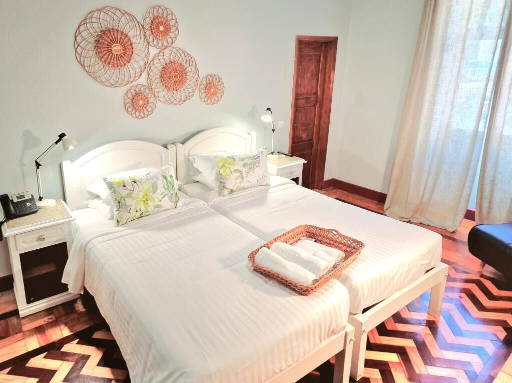 Een tweepersoonsbed met een wit hoofdeinde, een nachtkastje met een lamp, een houten vloer met een visgraatmotief en een muur met ronde decoraties.