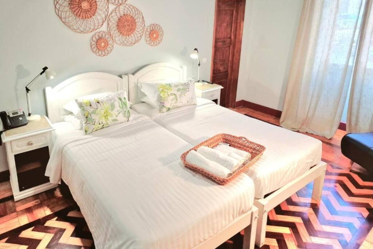 Een hotelkamer met twee bedden, een houten vloer, een wand met decoratieve cirkelvormige patronen, en een mand met handdoeken op het bed.