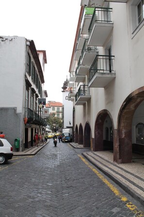 A narrow cobblestone street lined with multi-story buildings, some with balconies and arches. - Residencial Greco (Funchal)