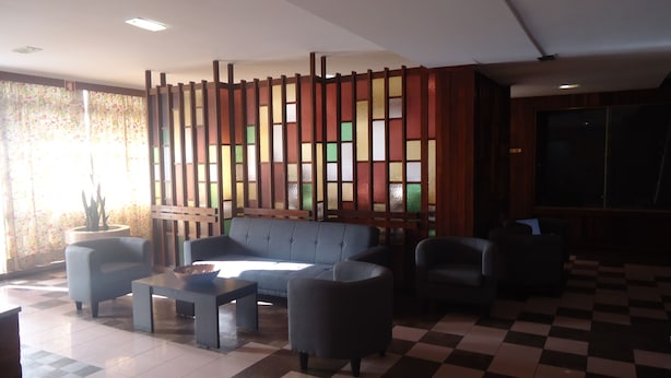 A modern lobby with a checkered floor, a sofa, armchairs, a coffee table, and a decorative partition with colorful panels.
