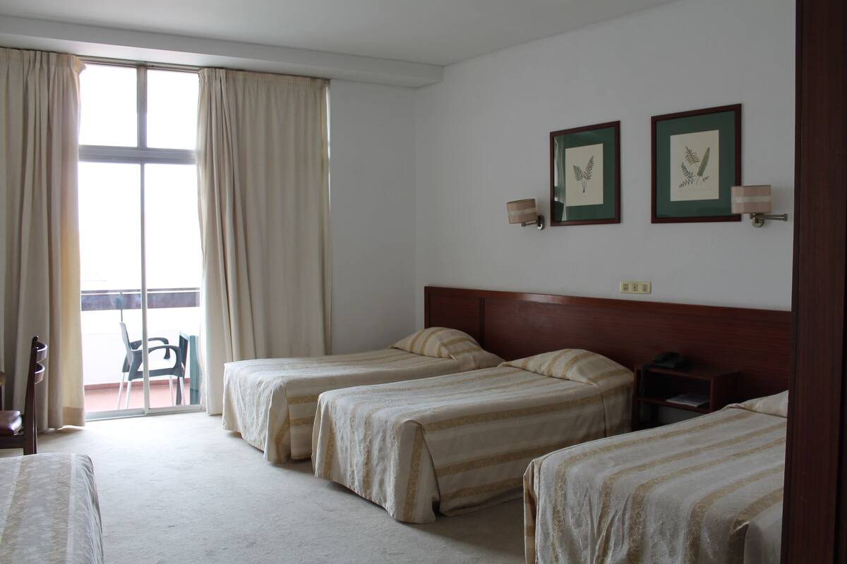 Et hotelværelse med to enkeltsenge, en stol, et lille bord og et vindue med gardiner.