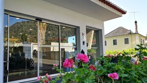 Een hotelentree met grote glazen deuren, een bordje met een 3-sterren beoordeling, en een tuin met roze bloemen op de voorgrond.