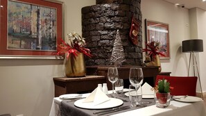 A dining area with a stone fireplace, framed artwork, and a red chair.