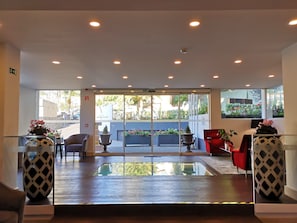 A reception area with a glass door leading to a garden, two red chairs, a large vase, and a potted plant.