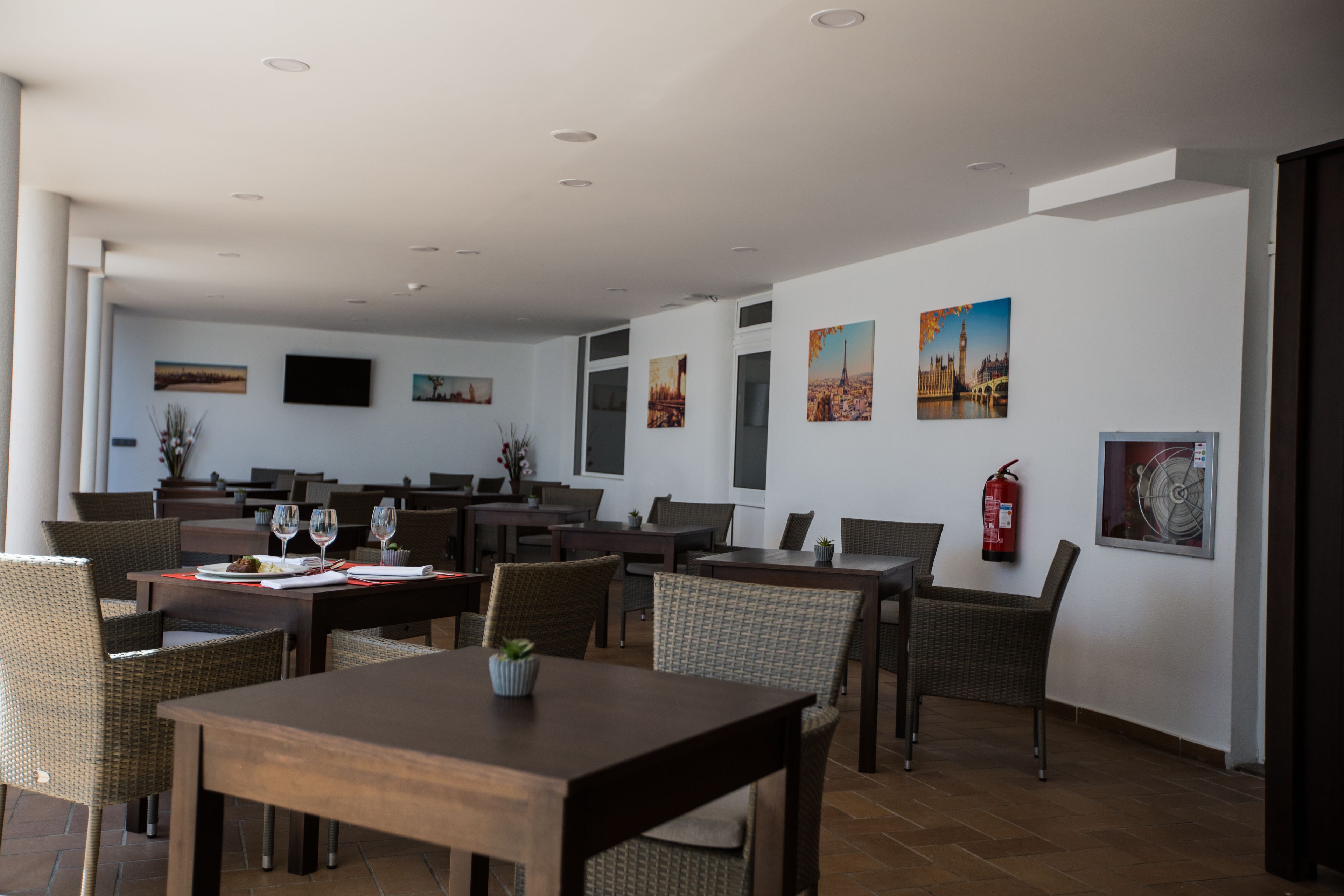 A spacious indoor dining area with multiple tables and chairs, a fire extinguisher on the wall, and various artworks displayed.