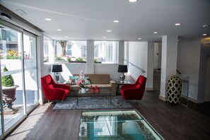A modern living room with a glass coffee table, red chairs, a beige sofa, and a view of a garden through large windows. - Santa Cruz Village Hotel (Santa Cruz)