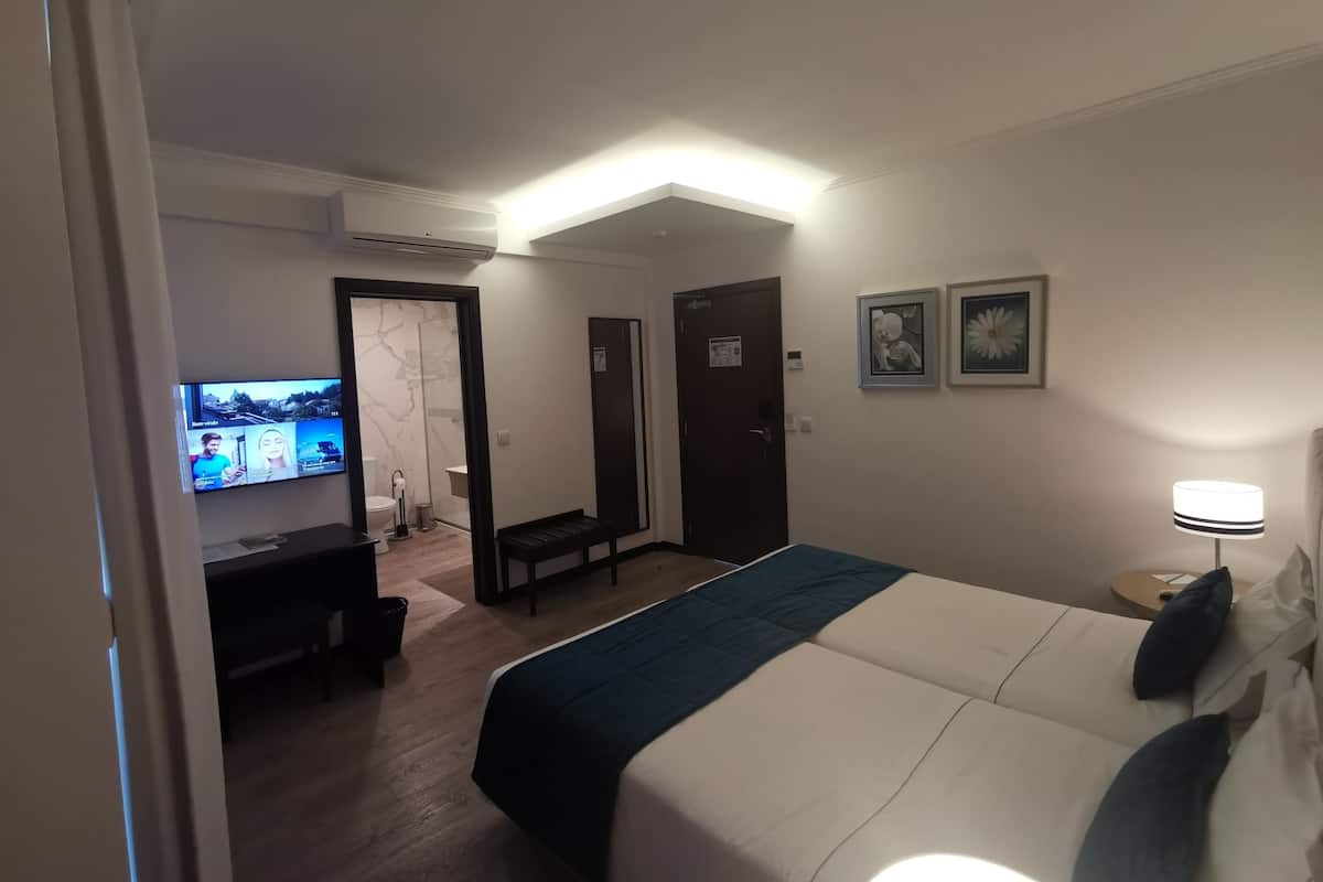 A hotel room with a bed, a desk, a television, and a bathroom visible through an open door.