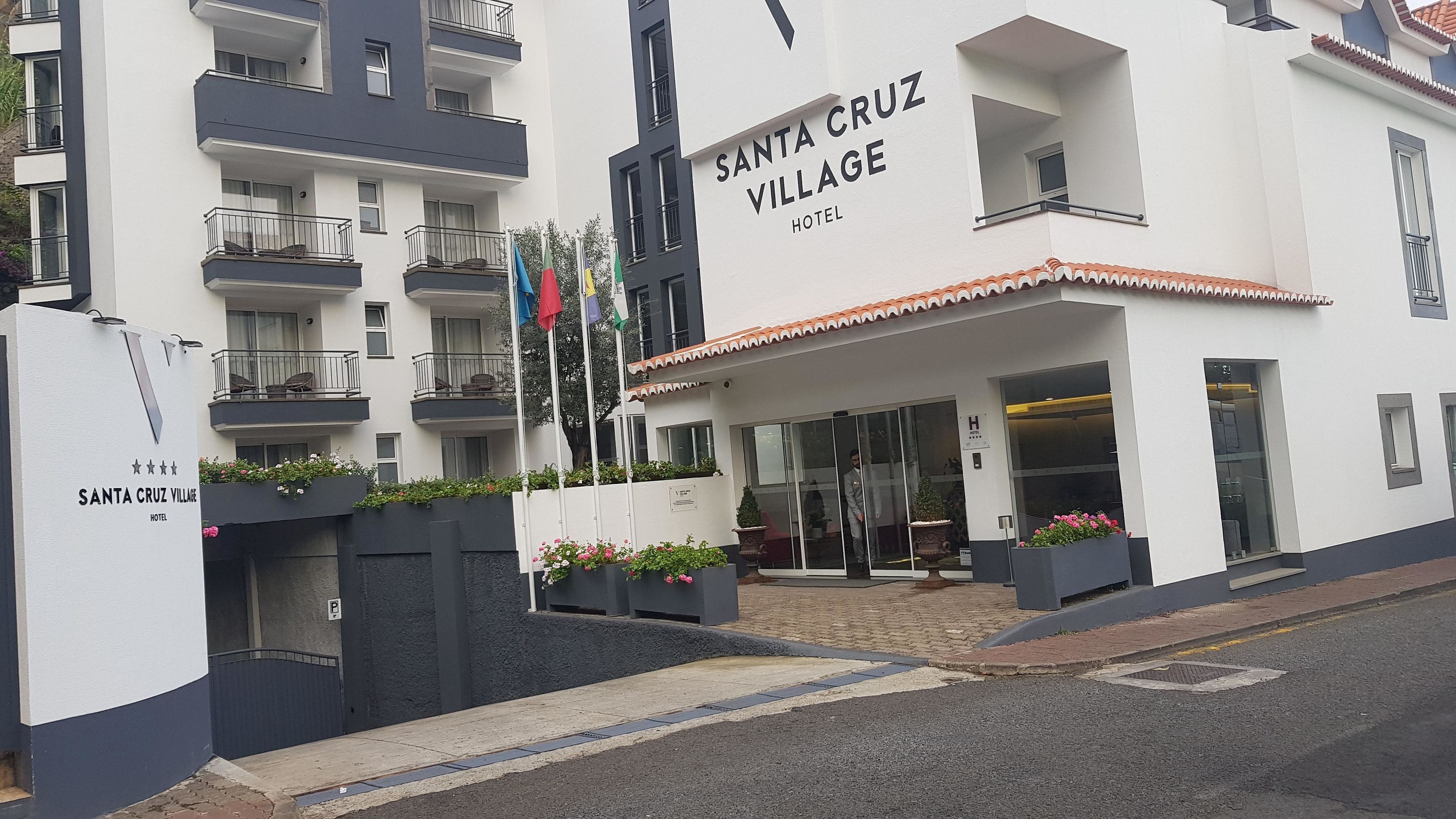 Un hôtel moderne appelé Santa Cruz Village, avec une façade blanche, des balcons et une entrée carrelée.