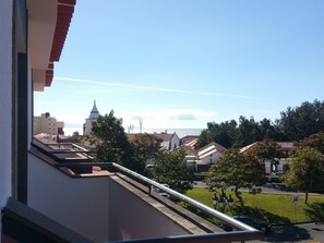 A balcony with a view of a church, residential buildings, and a parking area.