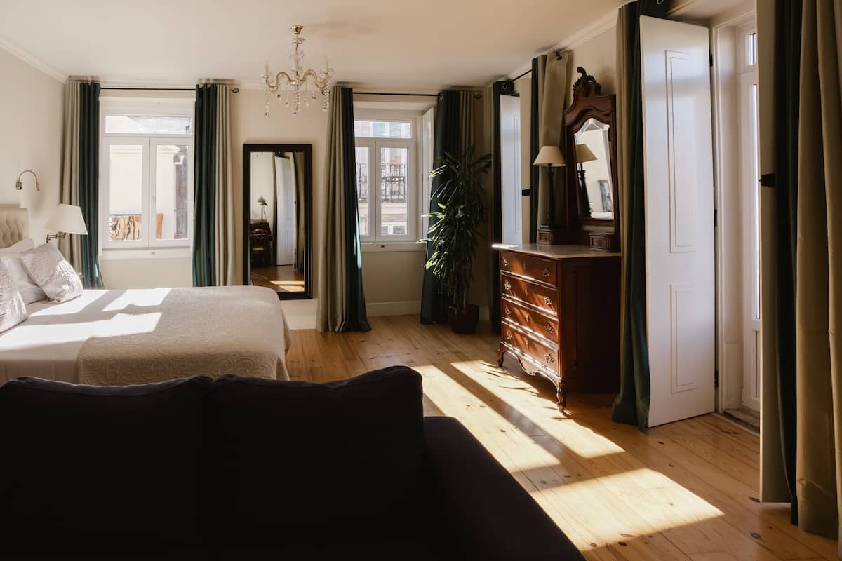 A well-lit bedroom with a large bed, a dresser, and a mirror. There is a potted plant and a chandelier.