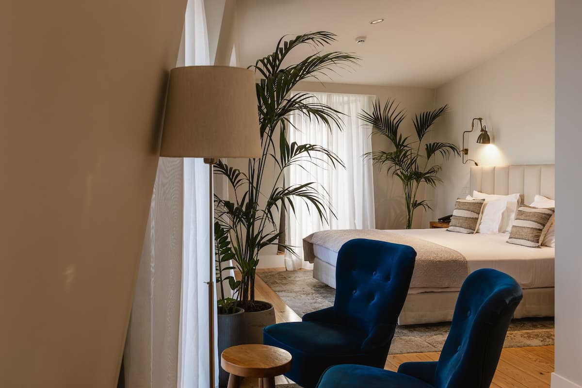 A bedroom with a bed, a blue armchair, a lamp, and two potted plants.