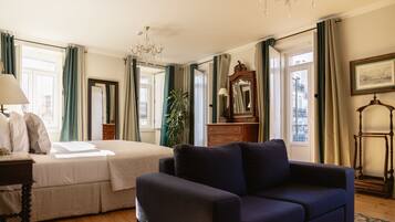 A bedroom with a bed, a blue sofa, a dresser, a mirror, and a chandelier.