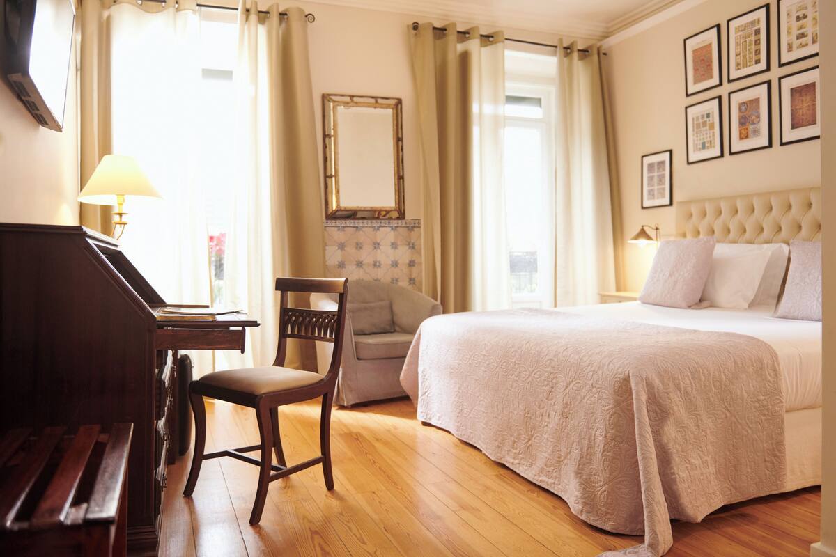 A hotel room with a bed, a chair, a desk with a lamp, and a piano.