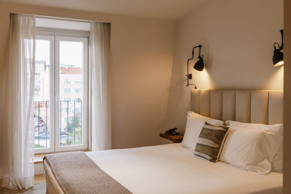 A hotel room with a large bed, a bedside table with a phone, and a window with curtains.