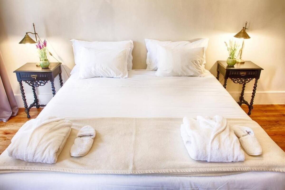 A neatly made bed with white linens, two bedside tables with lamps, and towels on the bed.