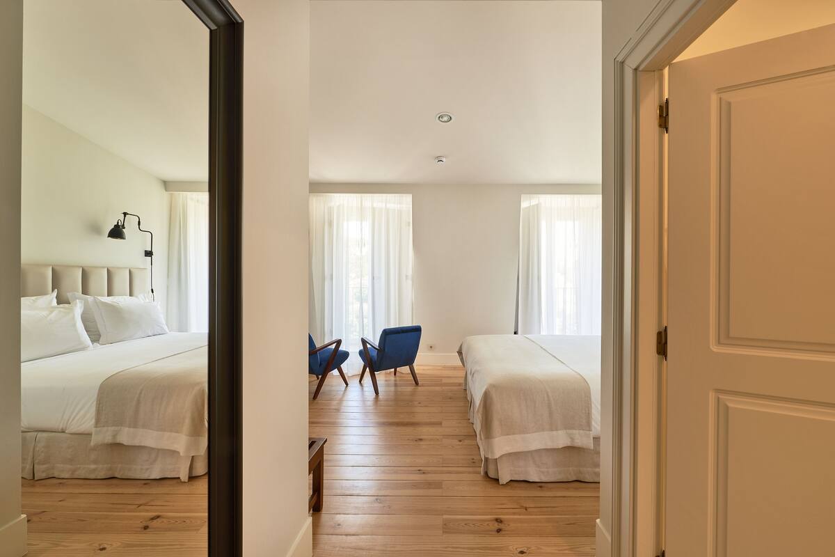 A hotel room with two beds, a wooden floor, a chair, and a nightstand.
