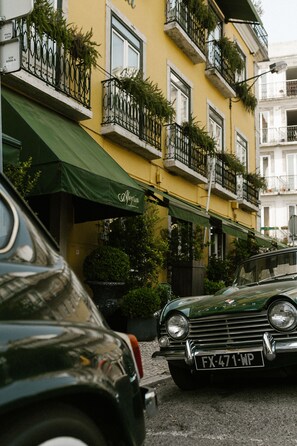 A yellow building with balconies, a green awning, and a car parked in front.