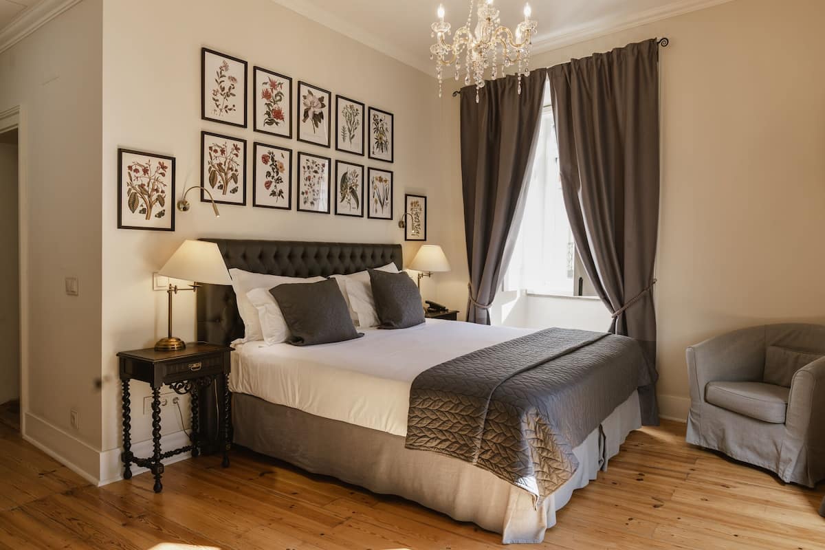 A bedroom with a large bed, two bedside tables, a chair, a chandelier, and framed botanical prints on the wall.