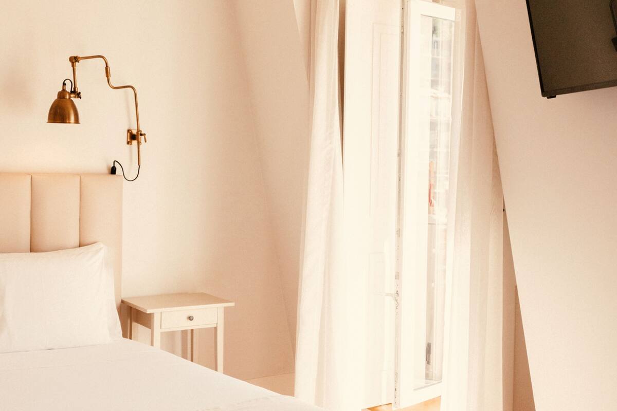 A bedroom with a bed, bedside table, lamp, and a view of the outdoors.