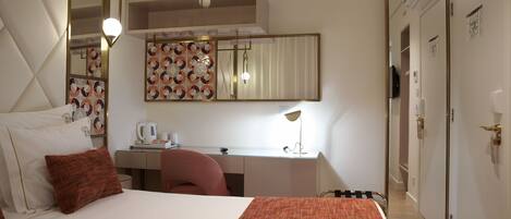 A hotel room with a large bed, a desk, a chair, a mirror, and a wardrobe.