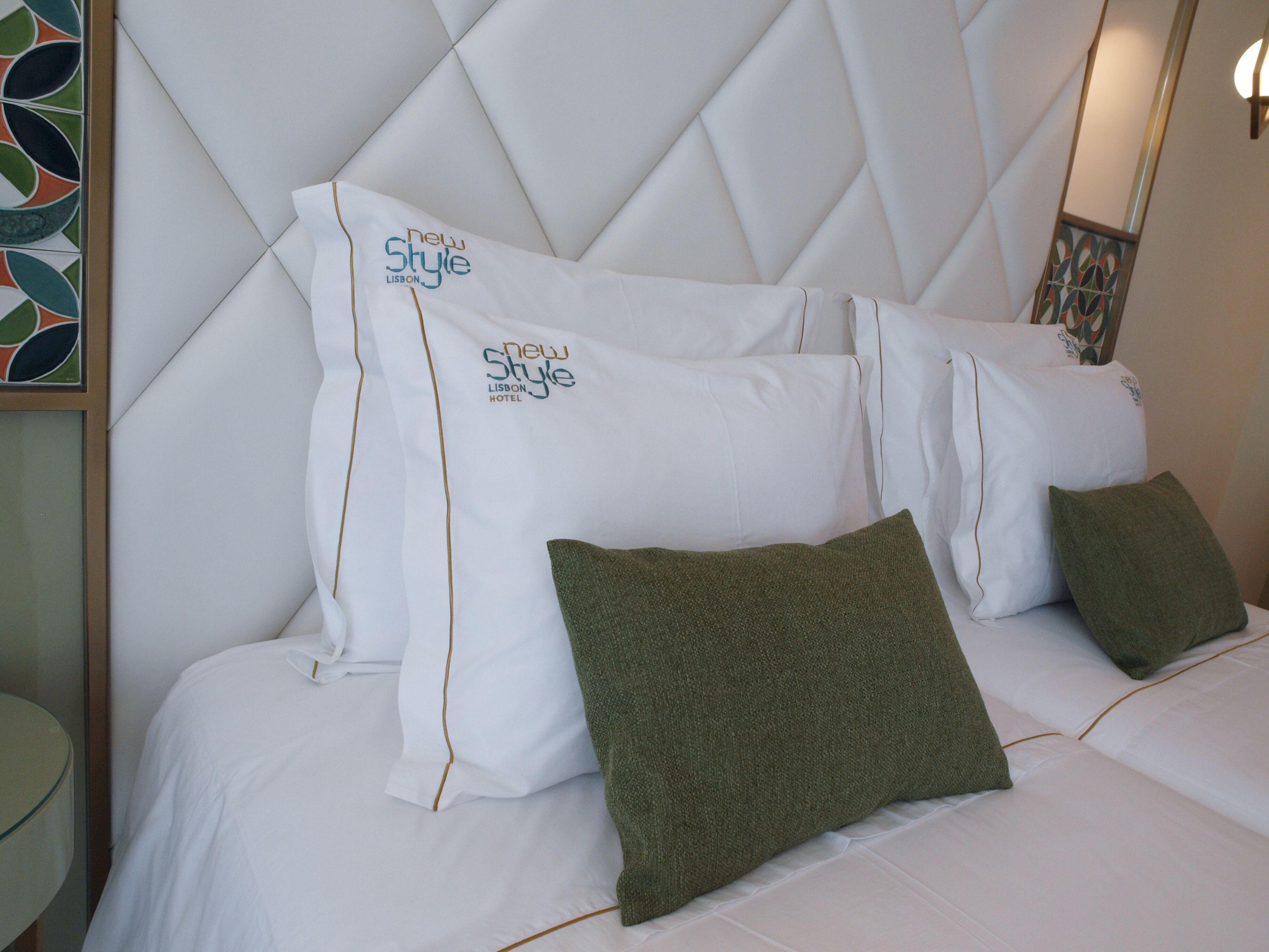 Habitación de hotel con cabecera capitonada, ropa de cama blanca y almohadas verdes.