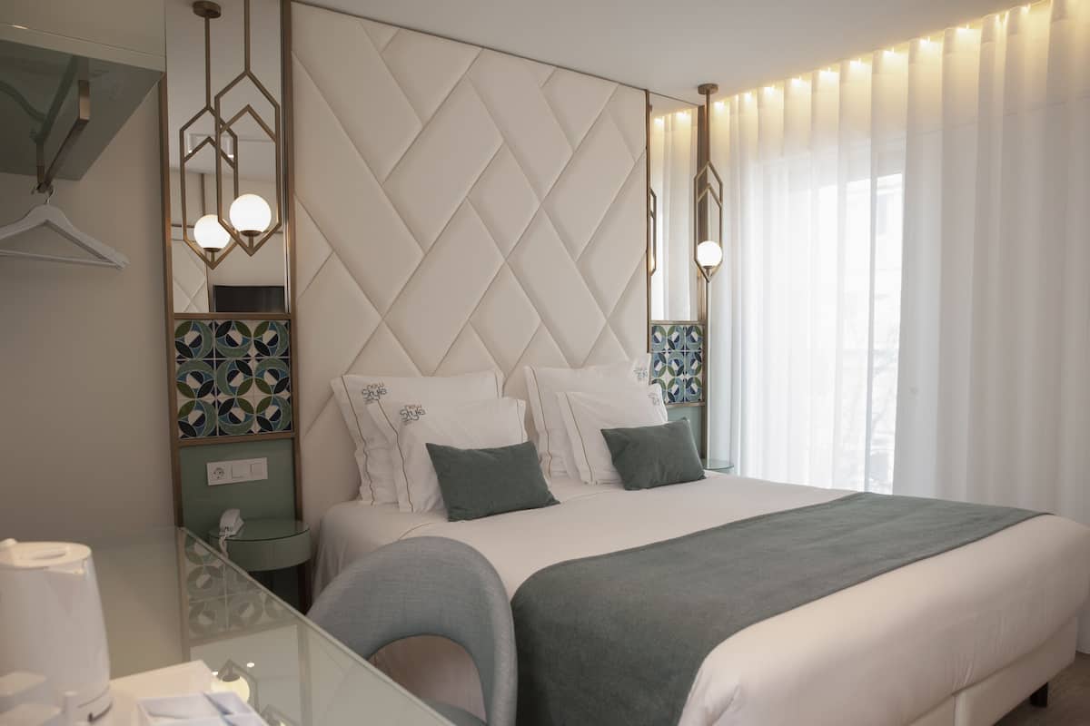 Quarto de hotel moderno com uma cama grande, uma mesa de vidro e cabeceira decorativa.